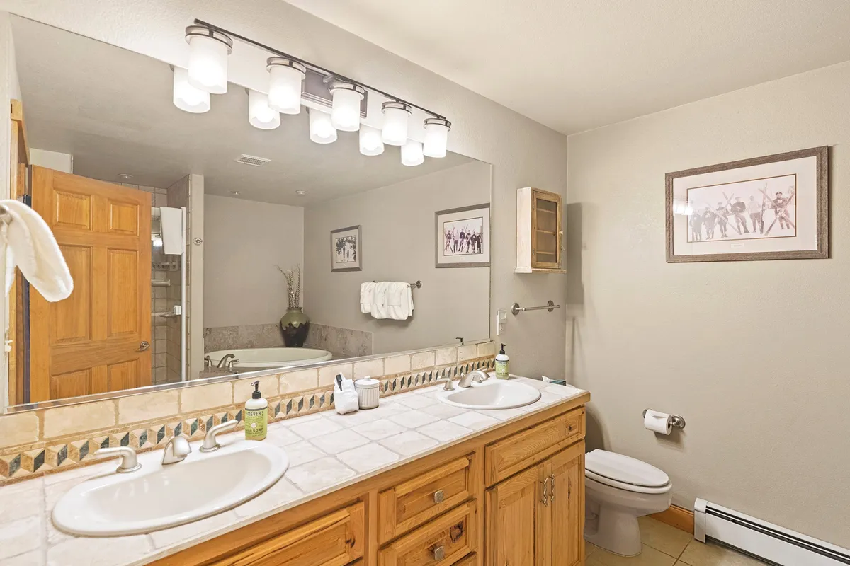 A spacious bathroom with a double sink vanity, large mirror, wooden cabinetry, and framed artwork. The organized, calming environment is ideal for family morning or bedtime routines, reflecting the shared bathroom described in the section.