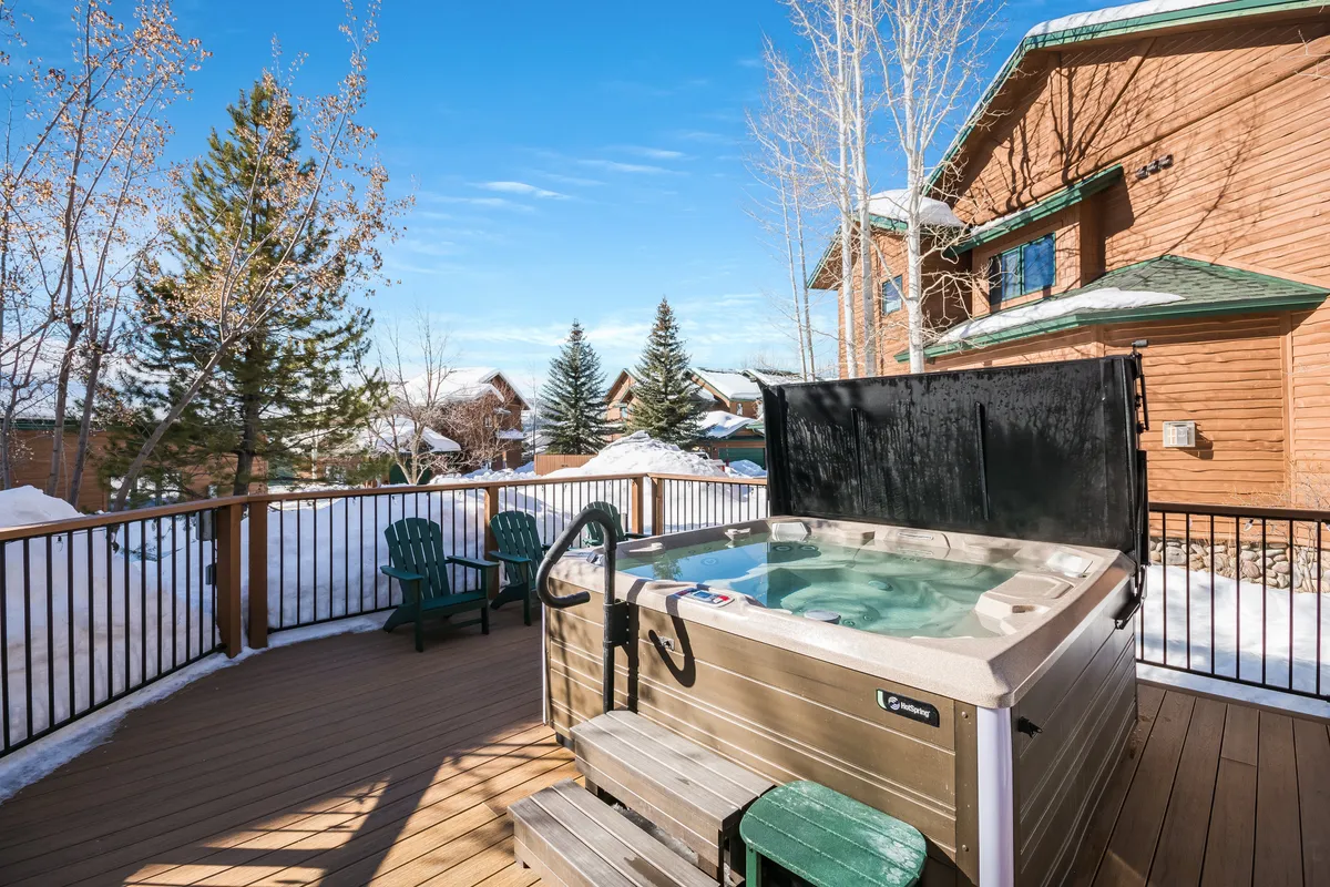 This exterior image captures another view of a hot tub on a spacious deck, set against sweeping mountain views. Outdoor seating and a fire pit nearby suggest opportunities for socializing and relaxation, while the warm light hints at sunset. The scene is vibrant, communal, and rejuvenating.