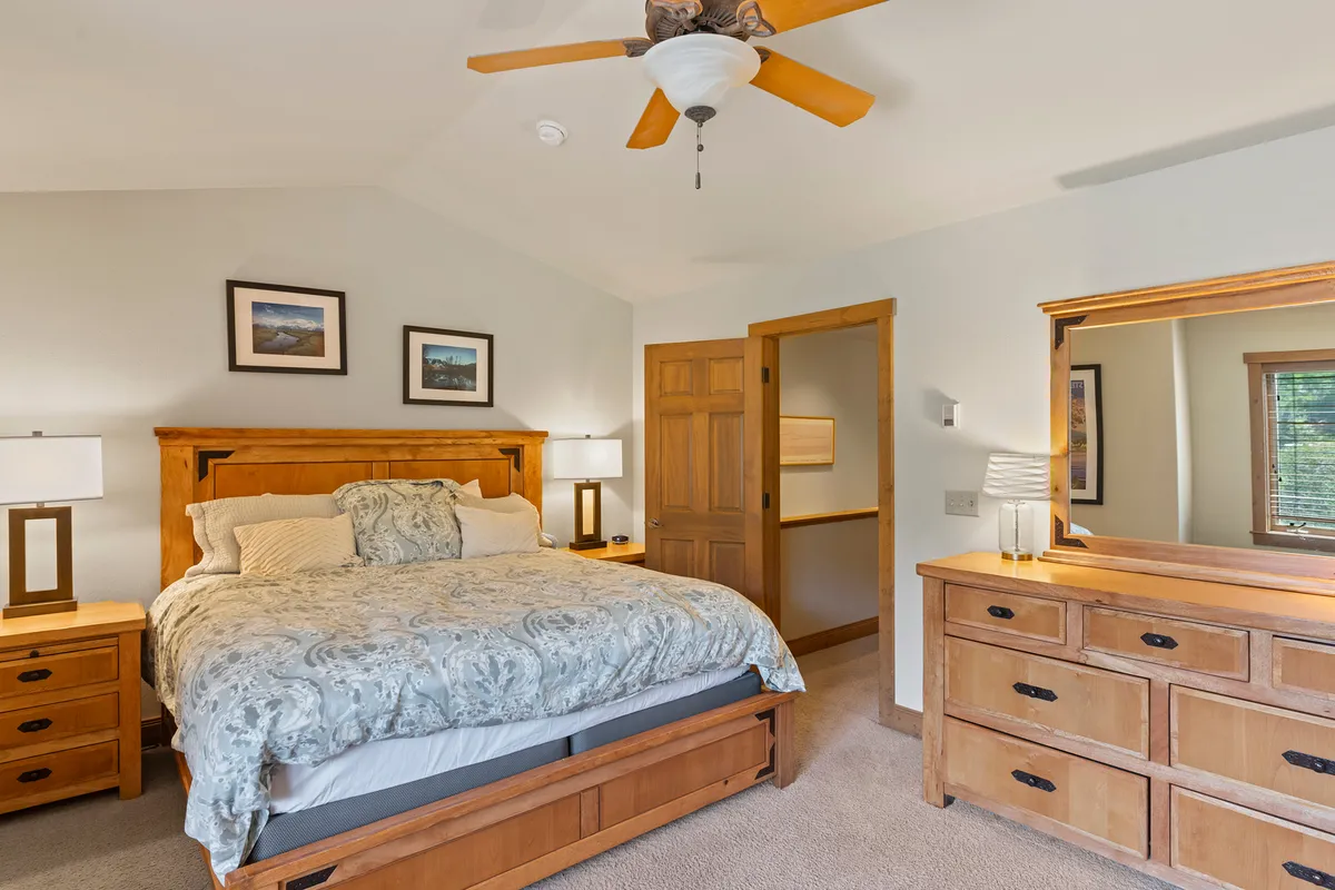 A cozy bedroom scene featuring a comfortable bed, dresser, ceiling fan, and framed art, all bathed in soft natural light. The inviting space promises restful nights after a full day in the snow, with a tranquil atmosphere for both adults and children.