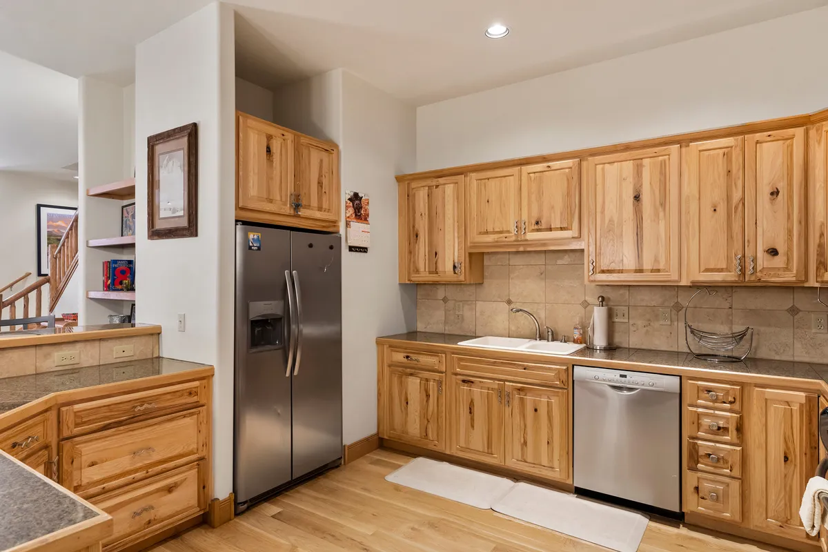 A warm, welcoming kitchen with natural wood cabinetry, stainless steel appliances, and granite countertops. The space is inviting and ideal for après-ski family dinners, entertaining, or gathering for hot cocoa after a day outdoors.