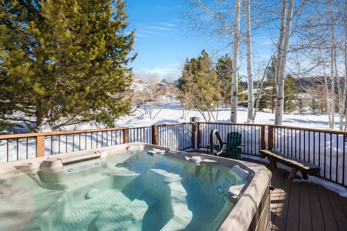This image features a community hot tub set on a deck surrounded by a snow-covered landscape and tall trees. The inviting steam rising from the hot tub contrasts beautifully with the wintry backdrop, hinting at relaxation and post-adventure unwinding. The overall mood is tranquil, with a clear sense of community and seasonal enjoyment.